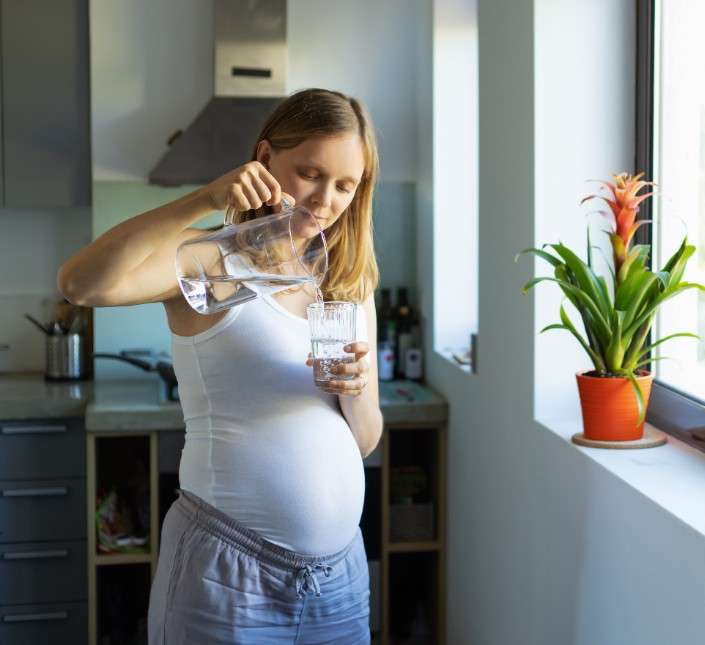 Mulher grávida a deitar água filtrada por osmose de um jarro na cozinha.