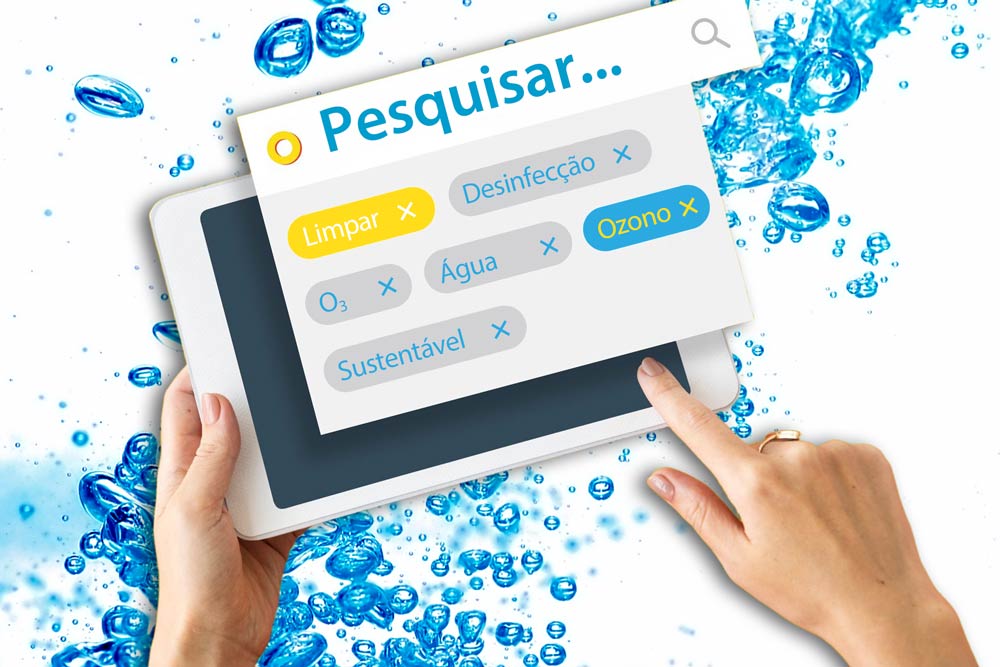 Fotomontagem com um fundo de bolhas de água azul e mãos em primeiro plano que seguram e manipulam um tablet com uma imagem de pesquisa com as palavras-chave "Ozono", "O3", "Limpo", "Desinfeção", "Água" e "Sustentável". A imagem é de cor clara e muito brilhante.